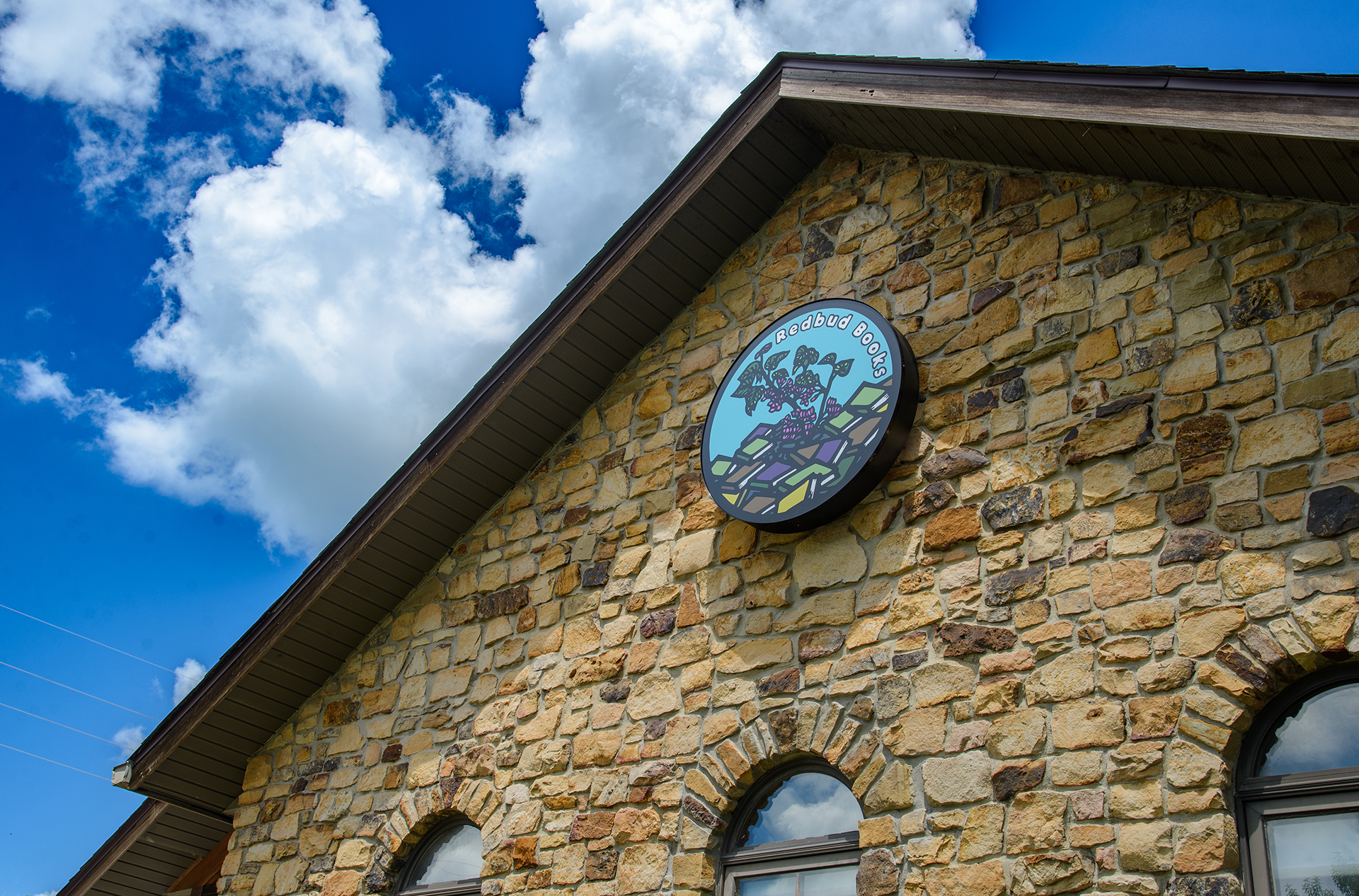 Round Redbud Books sign mounted on the bookstore’s stone facade